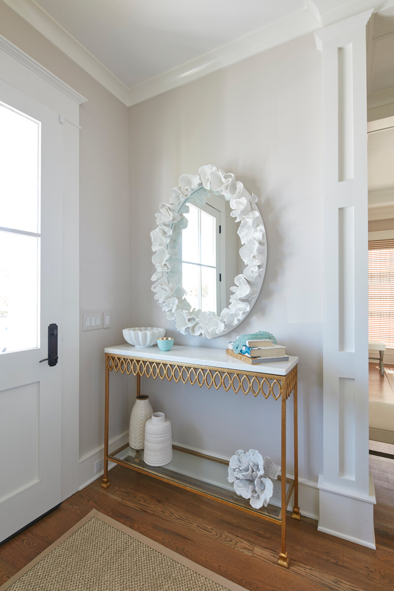 White entryway with white marble topped gold console and leaf coral mirror.